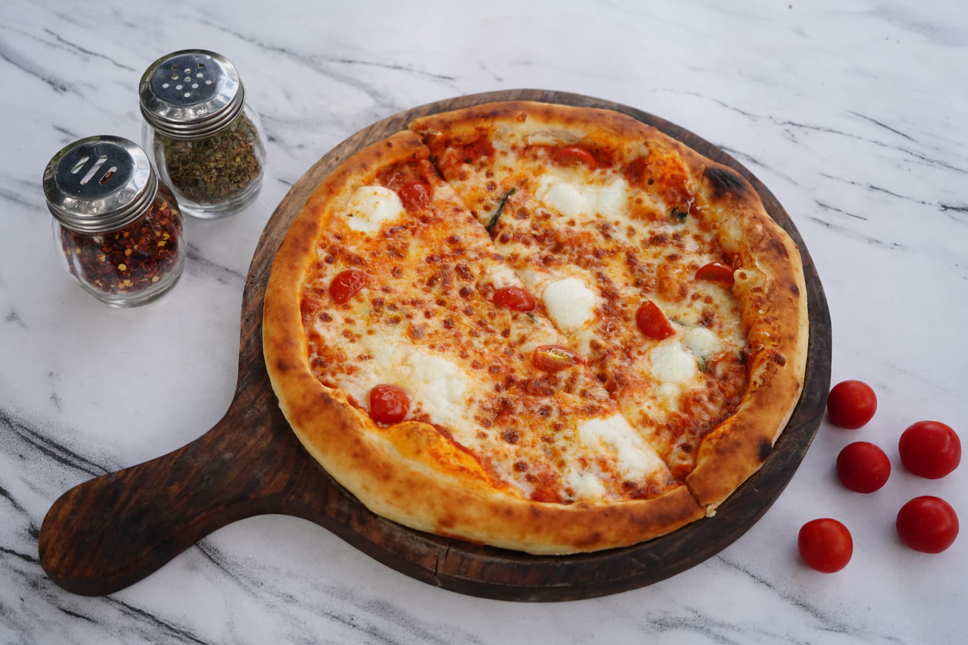 Margherita pizza with cherry tomatoes on a wooden paddle