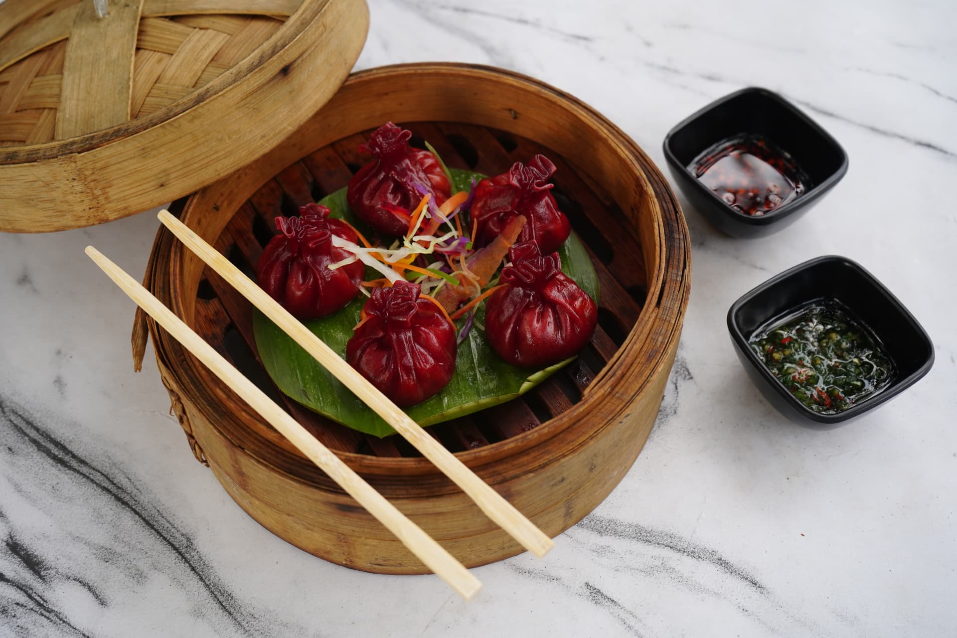 Beetroot dumplings in a bamboo steamer with dipping sauces